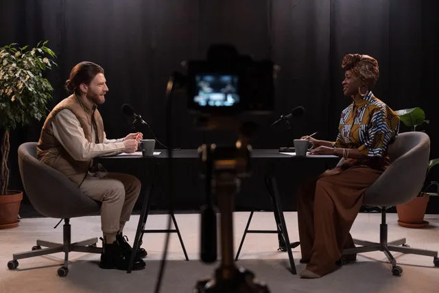 Two adults engaging in a podcast discussion in a studio with recording equipment. Creator-Kooperationen