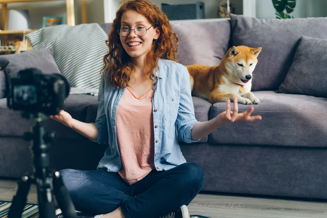 A smiling woman records a vlog with her Shiba Inu dog on a couch in a cozy living room setting. Rechte an Creator-Inhalten